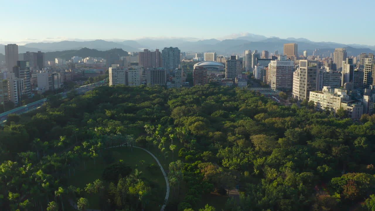 스카이라인으로 둘러싸인 푸른 나무가 있는 서사시 공중 비행 농촌 다안 공원 - 낮과 태양 동안 대만 타이페이 시, 배경에 있는 산의 실루엣