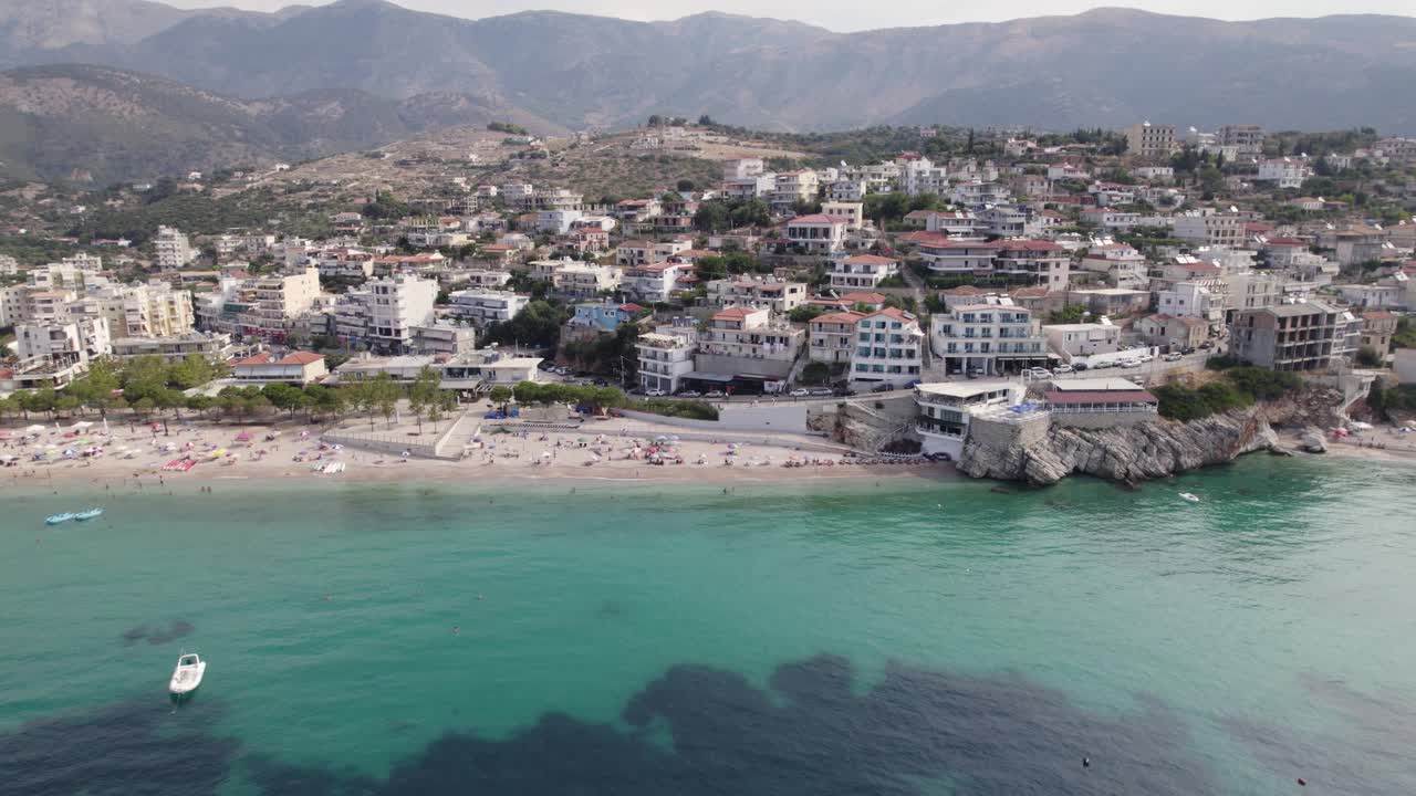 vista aérea de los edificios himare frente al mar por agua de color turquesa, montañas en el fondo, albania