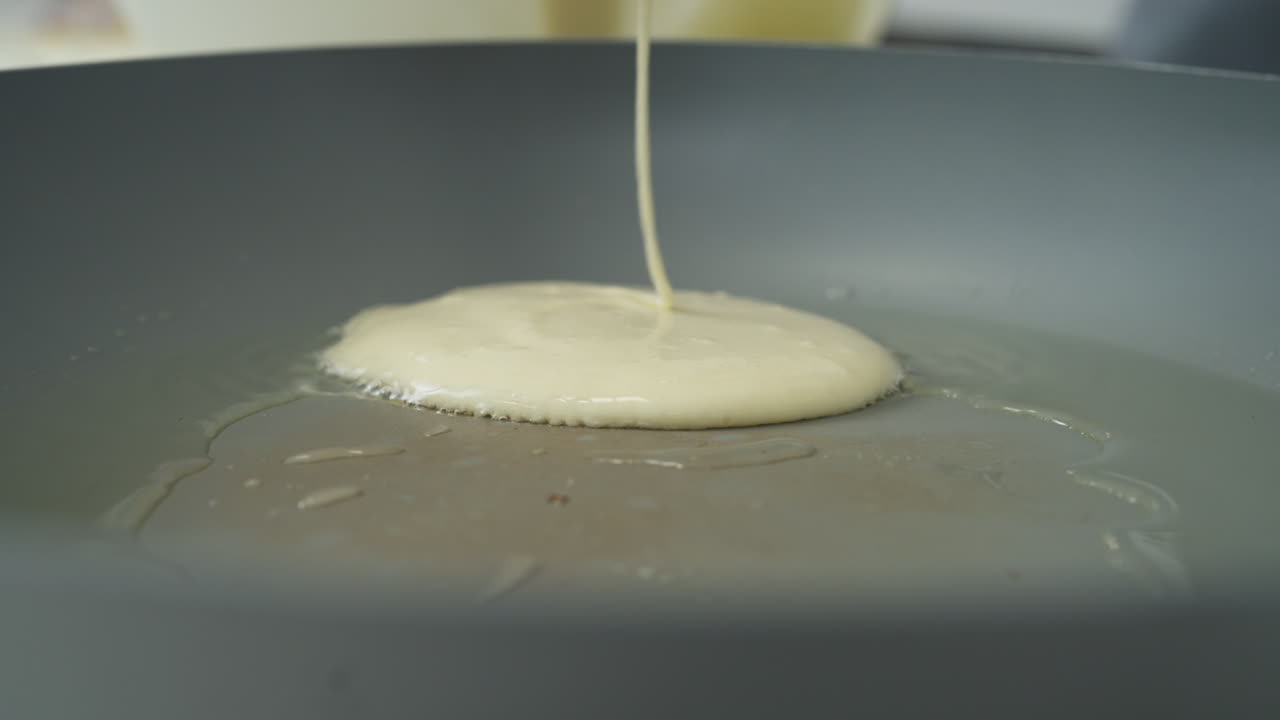 Close-up pouring sticky pancake batter into a hot frying pan