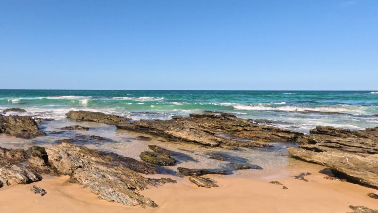 las olas se estrellan en la playa rocosa bajo un cielo despejado