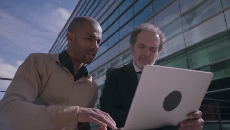 multiethnic colleagues discussing new projeсt on laptop outdoors