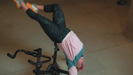 chica atlética hace trucos acrobáticos en bicicleta haciendo ejercicio en una máquina de ciclismo estacionaria en el interior