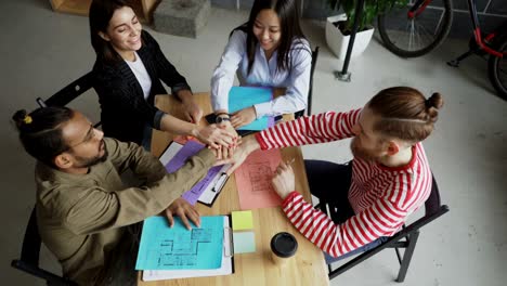 top view of young multi-ethnic team crossing hands together after successful agreement about new project in modern loft office