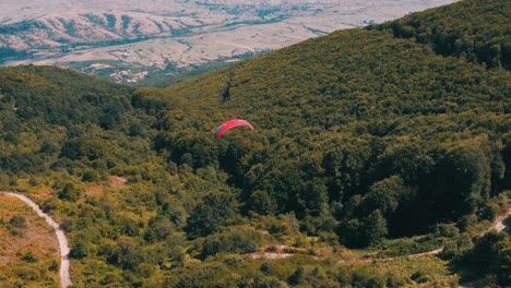 Aerial-shot-of-a-paraglider-flying-over-a-forest