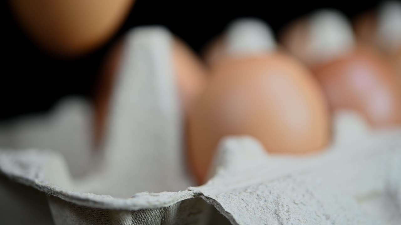 Eggs being carefully placed by three fingers in the empty pockets of the tray made of paper