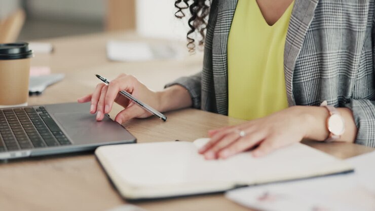 Woman, hands and writing in book by laptop