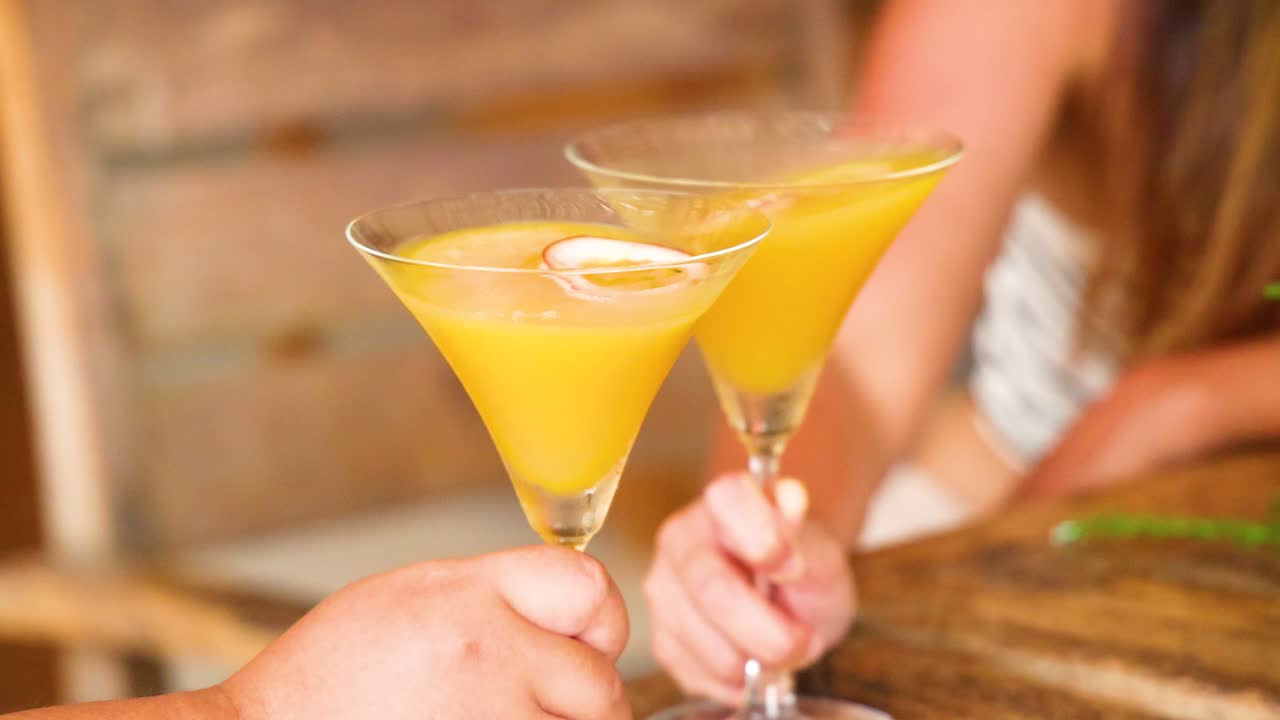 Due persone che brindano con cocktail gialli in un'atmosfera calda e invitante con illuminazione soffusa e sfondo in legno.