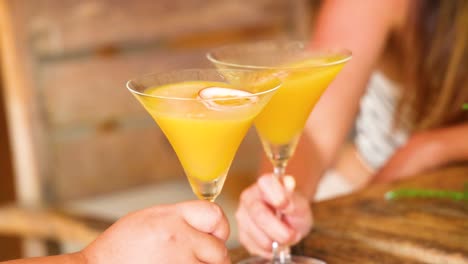two people clinking yellow cocktails in a warm, inviting atmosphere with soft lighting and wooden background