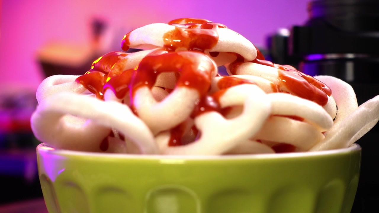 Nærbillede videooptagelse af sauce, der falder ned på en grøn skål med mexicanske friturestegte hjul.