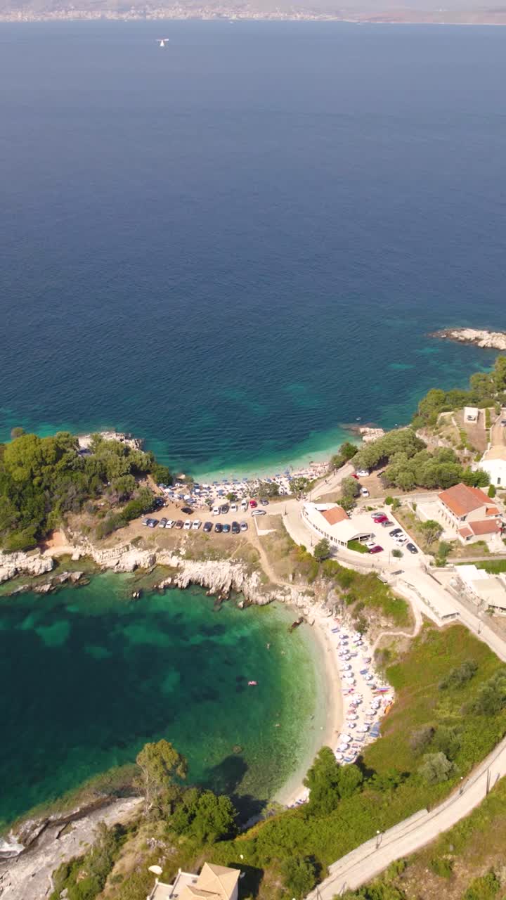 Vertical aerial view of the rocky small beaches along the Kassiopi coastline in Corfu, showcasing turquoise waters and rugged shoreline
