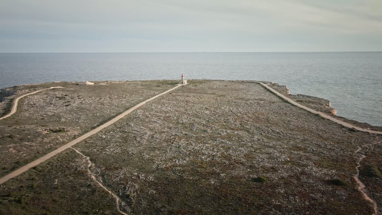 Aerial footage gliding forward above rocky coastal terrain toward a solitary lighthouse overlooking the ocean. Perfect for travel, nature, and maritime themes