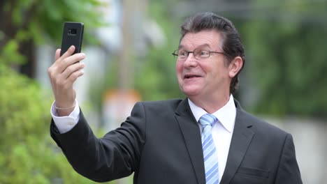 happy handsome senior businessman video calling in the streets outdoors