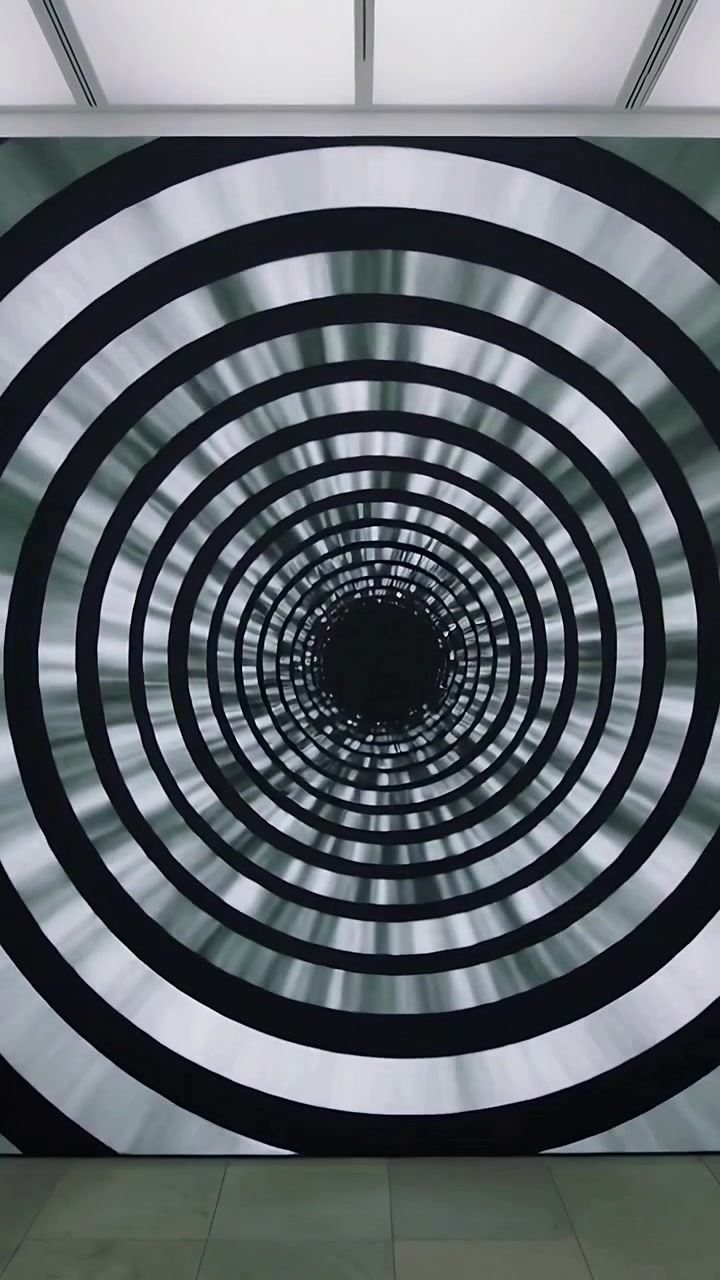 Video verticale: Display digitale a parete animato che ruota e pulsa, creando un effetto tunnel nella hall.