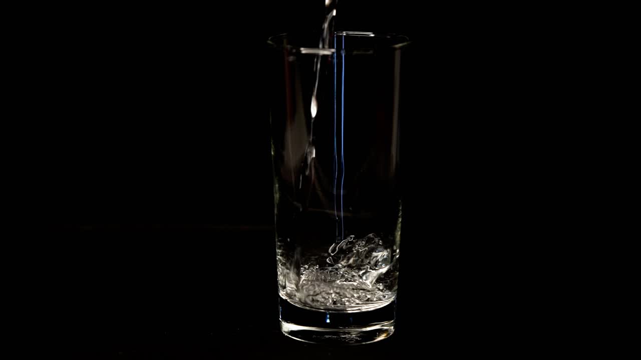 Hælder vand i et glas mod sort baggrund i slow motion.