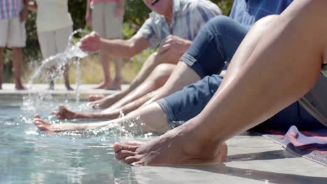 happy diverse senior friends with feet in pool at sunny garden party, unaltered, in slow motion