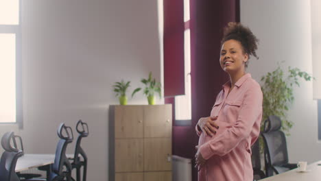 pregnant happy woman posing at camera while touching her belly in the office 1