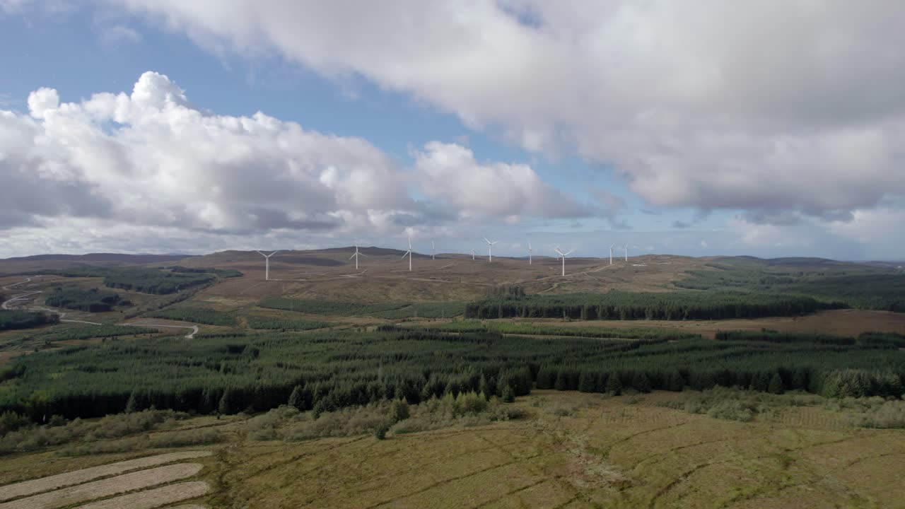 imágenes aéreas de drones que se elevan para revelar múltiples turbinas eólicas giratorias en un parque eólico escocés rodeado de plantaciones forestales de coníferas comerciales en la península de kintyre, argyll, escocia