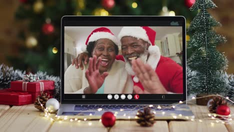 Pareja-De-Ancianos-Afroamericanos-Con-Sombreros-De-Santa-En-Videollamada-En-Una-Computadora-Portátil,-Con-árbol-De-Navidad