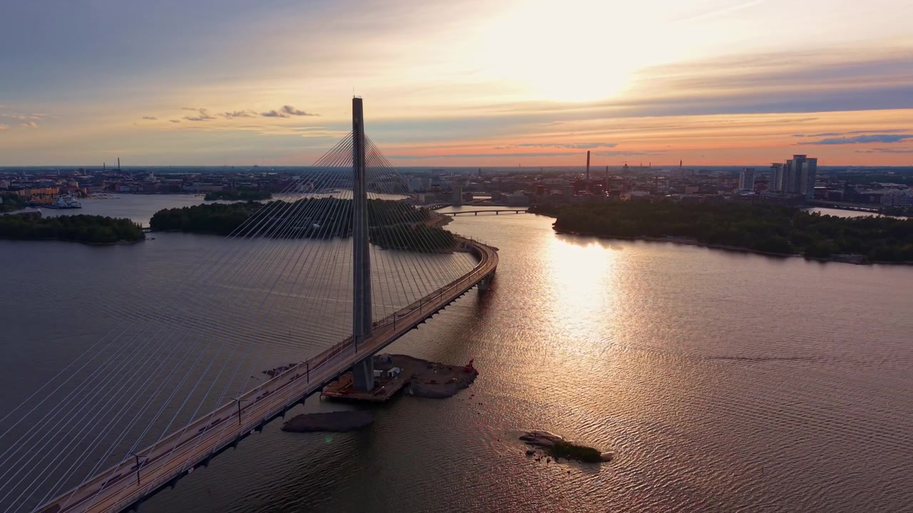 Ponte strallato Kruunuvuorensilta che attraversa la baia di Helsinki al tramonto, con luce dorata che si riflette sull'acqua calma e lo skyline della città sullo sfondo, Finlandia.