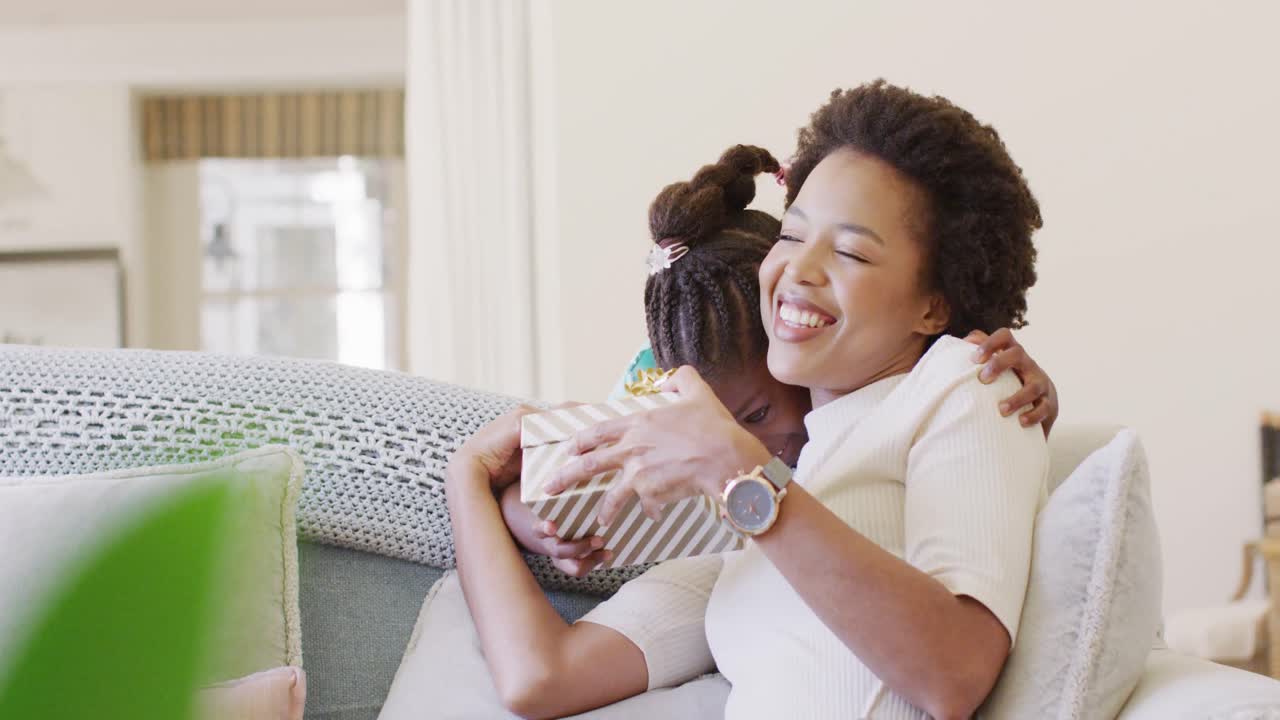 Smiling african american daughter giving happy mother a mother's day gift, slow motion