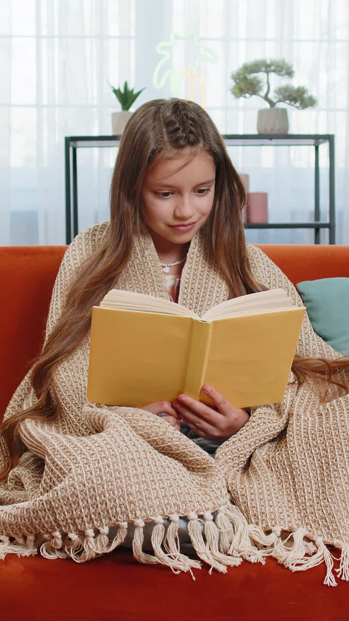 Girl wrapped in blanket relaxing reading book turning pages smiling enjoying literature education