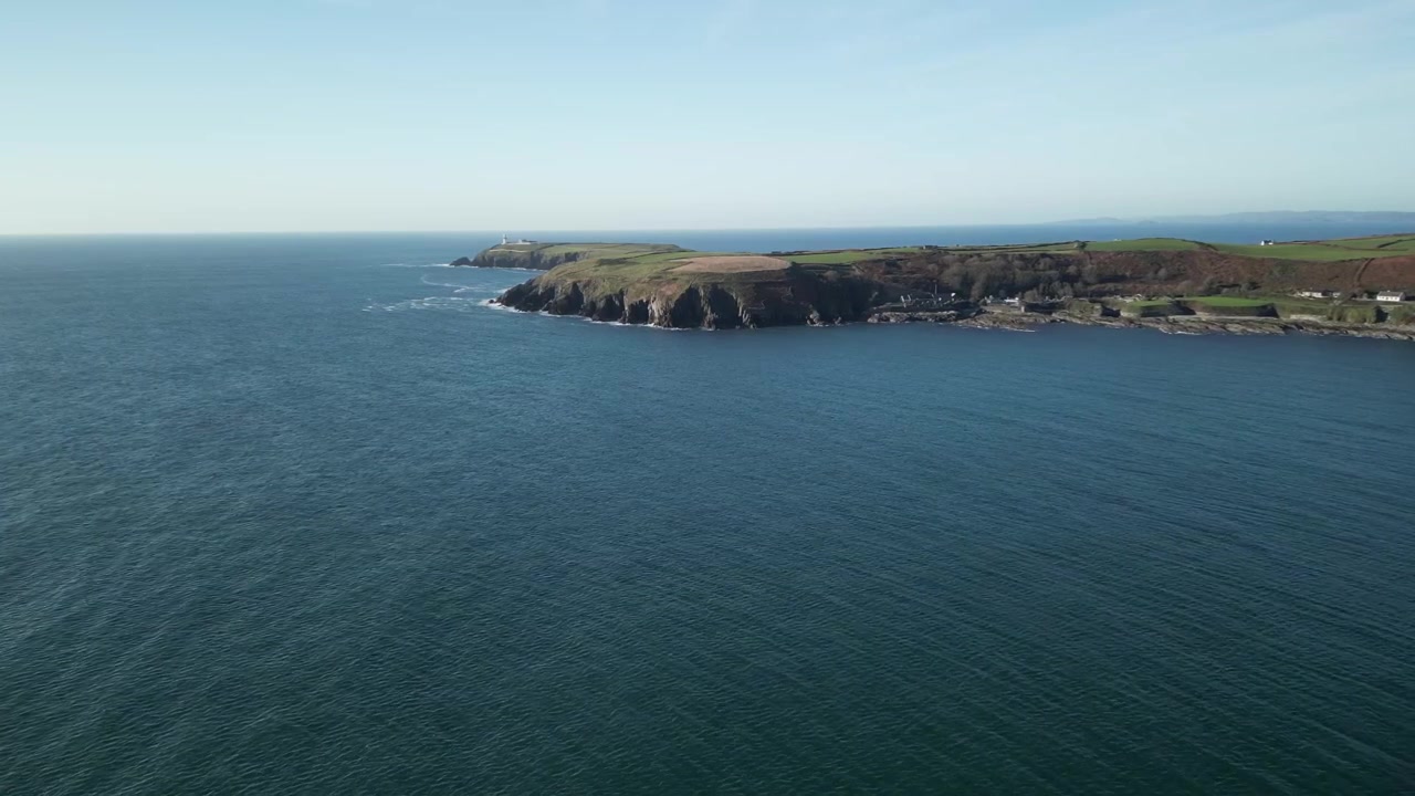 Batı Cork'ta uzaktaki burun ve güneşli bir günde geniş, sakin Atlantik Okyanusu, İrlanda'daki engebeli, çıkıntılı kıyıya doğru uçan bir drone'un havadan çekimi