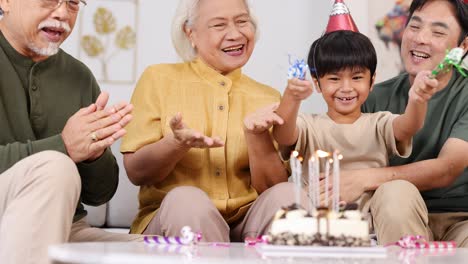an elderly family joyfully celebrates a birthday with cake, candles, and party hats in a warmly lit home