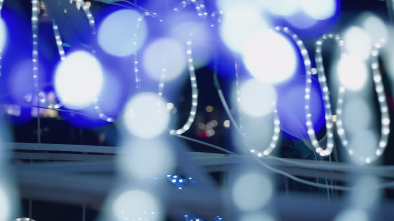 A blurred shot showing festive Christmas lights, with a person in the background partially visible, as soft, glowing light strands create a dreamy atmosphere in an urban setting at night