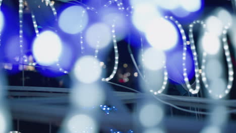 a blurred shot showing festive christmas lights, with a person in the background partially visible, as soft, glowing light strands create a dreamy atmosphere in an urban setting at night