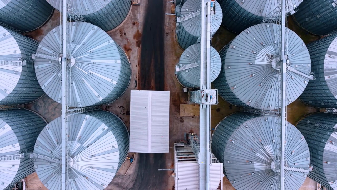 Bird's eye view of grain silos in a rural area during the day. Large group of circular grain silos in a farming area. The view captures their shapes and structure.