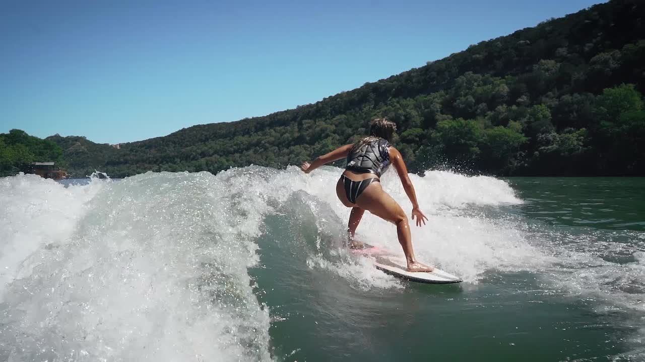 Female wakesurfer lands slow motion shove it trick on wake surf board on Lake Austin, Texas