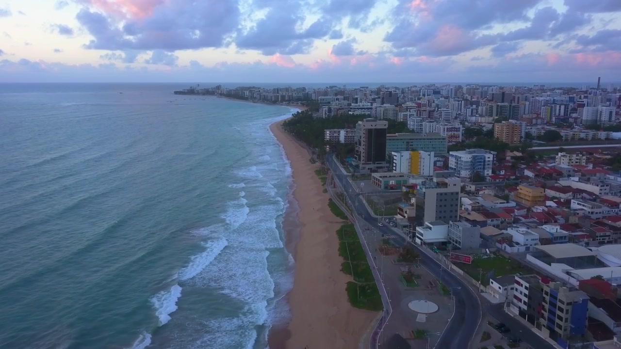 Deslizamiento aéreo panorámico lateral a lo largo de la costa de Maceió mientras un atardecer rosado ilumina el horizonte de la playa. Filmado en 4K a 25 fps.