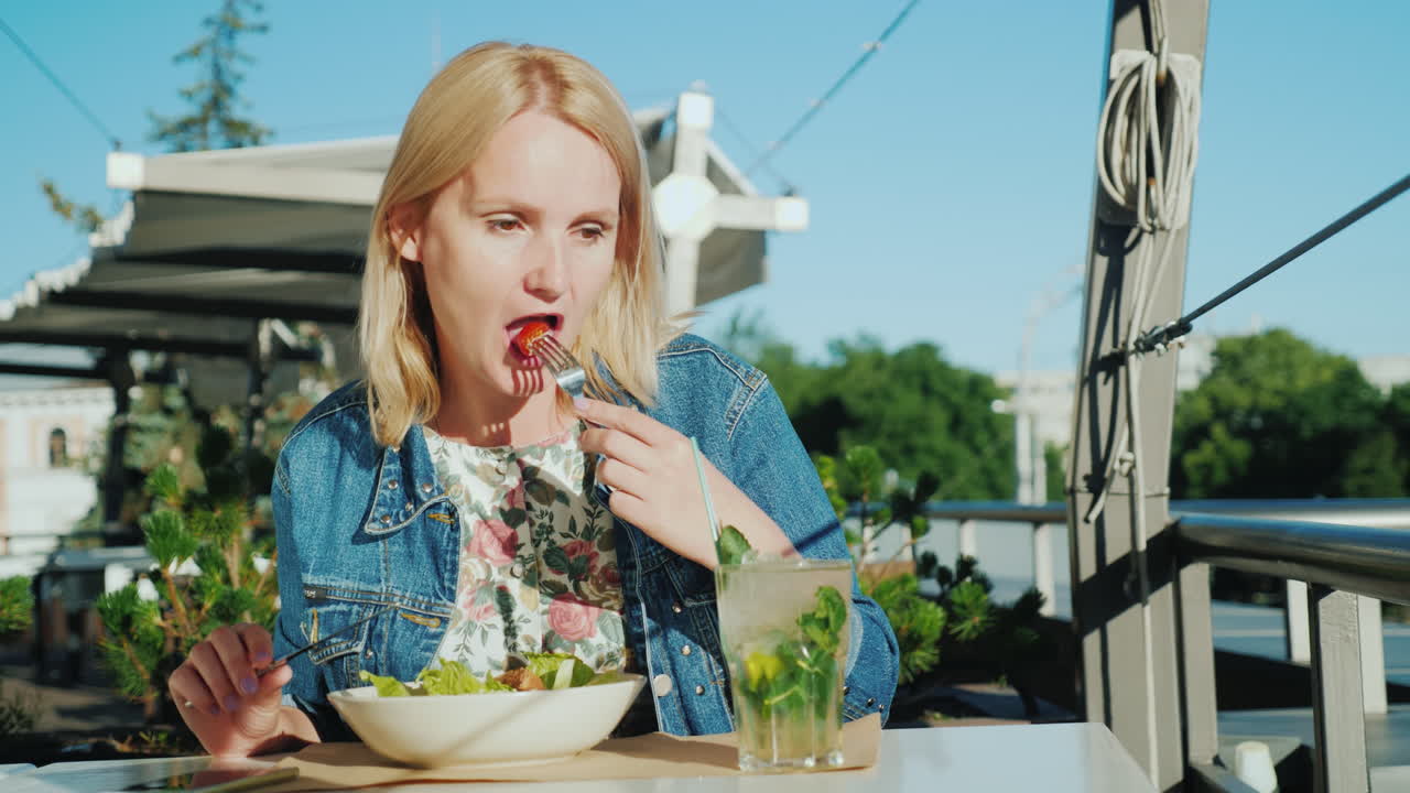 una mujer joven está comiendo una ensalada en la terraza de verano en un restaurante comer al aire libre 4k video