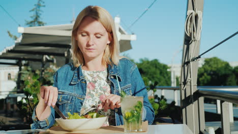 una mujer joven está comiendo una ensalada en la terraza de verano en un restaurante comer al aire libre 4k video