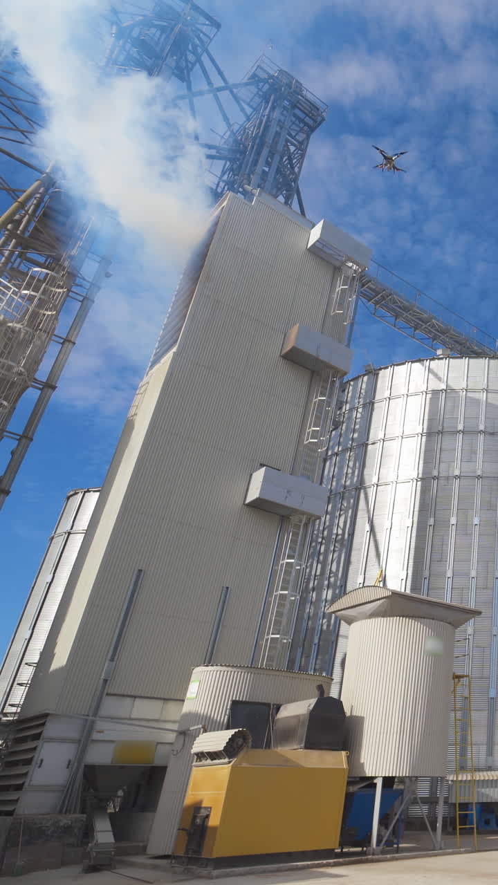 Panoramic view of agricultural plant. Large round grain elevators for storing grains. Thick fumes releasing into the air during grain processing on a factory. Vertical video