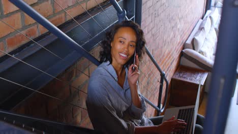 Woman-talking-mobile-phone-using-laptop-on-stair-4k