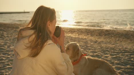 Una-Chica-Rubia-Bebe-Té-Caliente-De-Una-Taza-De-Termo-En-Una-Playa-Soleada-Por-La-Mañana.-Cerca-De-La-Niña-Está-Su-Gran-Y-Lindo-Perro-De-Color-Claro