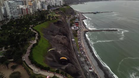 Aerial-tilt-up-shot-shows-a-couple-of-paragliders-flying-over-a-coastal-ravine-at-the-coastline-of-the-city