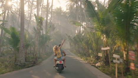 happy couple riding scooter on tropical island girlfriend having fun with arms raised exploring beautiful travel destination on motorcycle with boyfriend