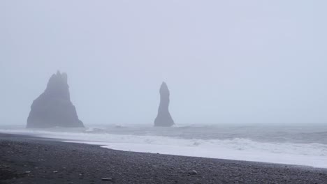 Wellen-Brechen-An-Einem-Schwarzen-Sandstrand-In-Island-Mit-Großen-Felsen-Im-Wasser---Zeitlupe