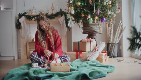 happy woman tying ribbon on wrapped christmas gift at home