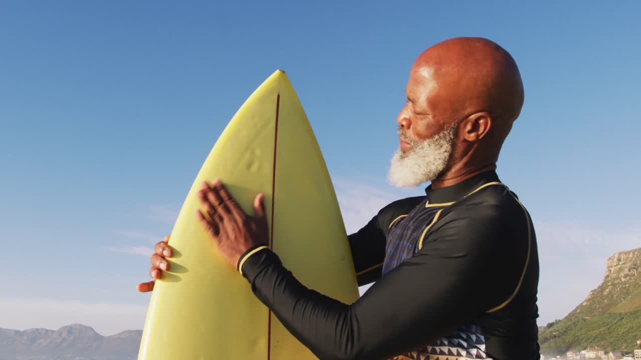 Eldre afroamerikansk mann som går med et surfebrett på stranden