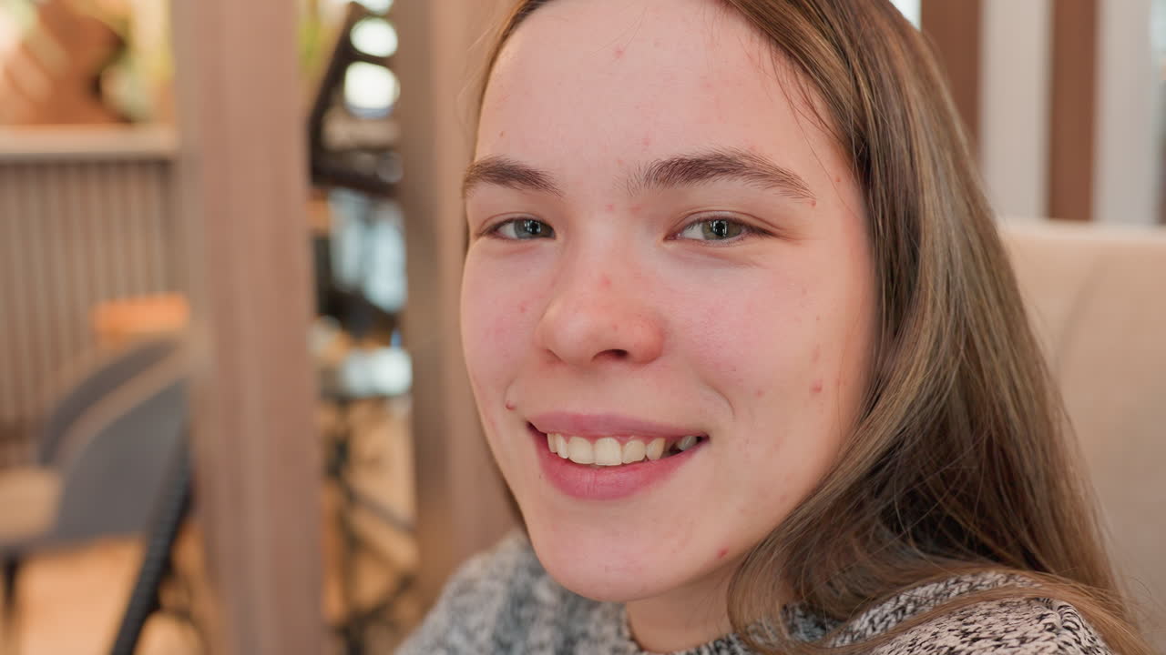 Female youth smiling happily while seated in cozy lounge featuring warm lighting and reflective mirror decor, capturing cheerful indoor moment filled with natural charm and relaxed modern ambiance