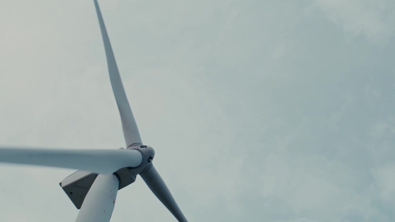 Mulino a vento che gira nel vento generando energia pulita in un campo, contro un cielo parzialmente nuvoloso, con stile e movimento fluido e cinematografico