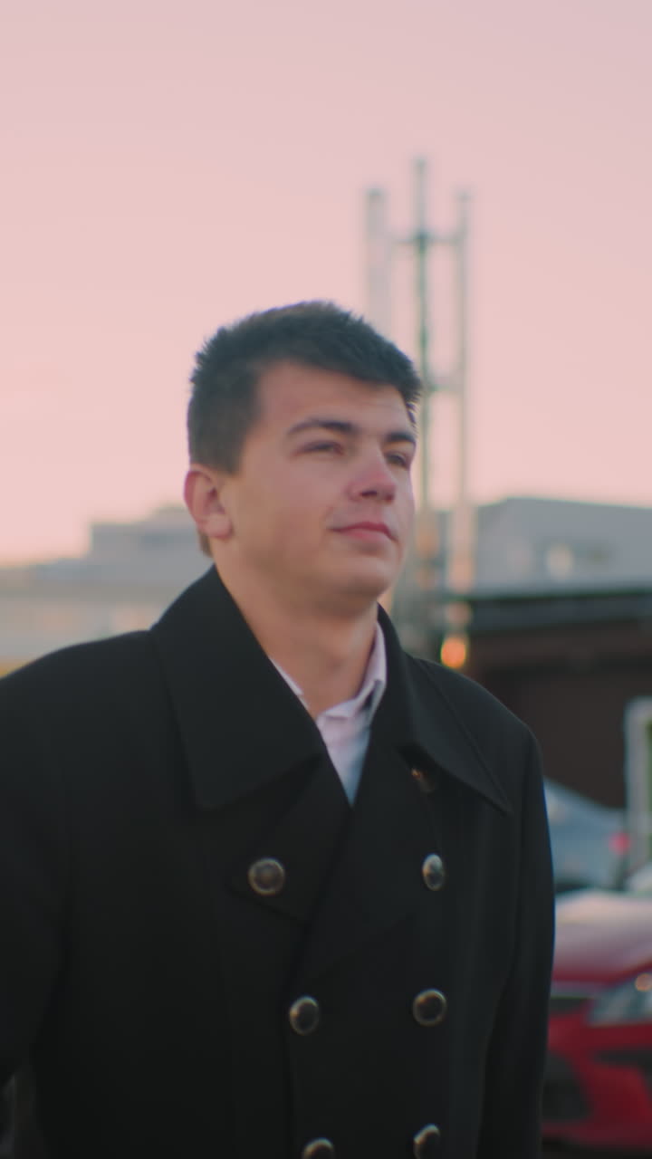 검은 코트를 입은 젊은이가 왼손에 브리프케이스를 들고 차 밖으로 나갑니다. 배경에는 주차된 자동차, 사무실 주거 건물, 하늘에 은 구름이 있습니다.