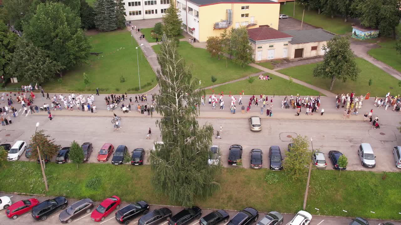 A ceremonial procession of people moves through the streets of Limbaži, with participants walking along the cobbled roads. The event creates a festive and community-focused atmosphere in the city.