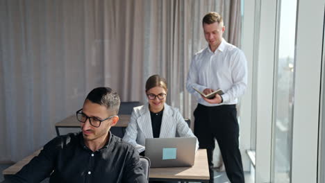 male manager checking information in his paper notebook standing near female employee. people using computers at their work in office.