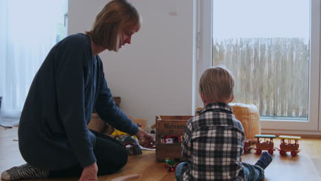 madre e hijo sentados en el suelo y construyendo un tren de juguete juntos