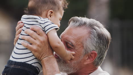 senior hispanic man talking to his baby grandson, holding him in the air, close up, side view