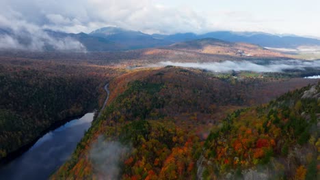 aerial view of clouds rolling in next to a lake in upstate new york surrounded with fall foliage